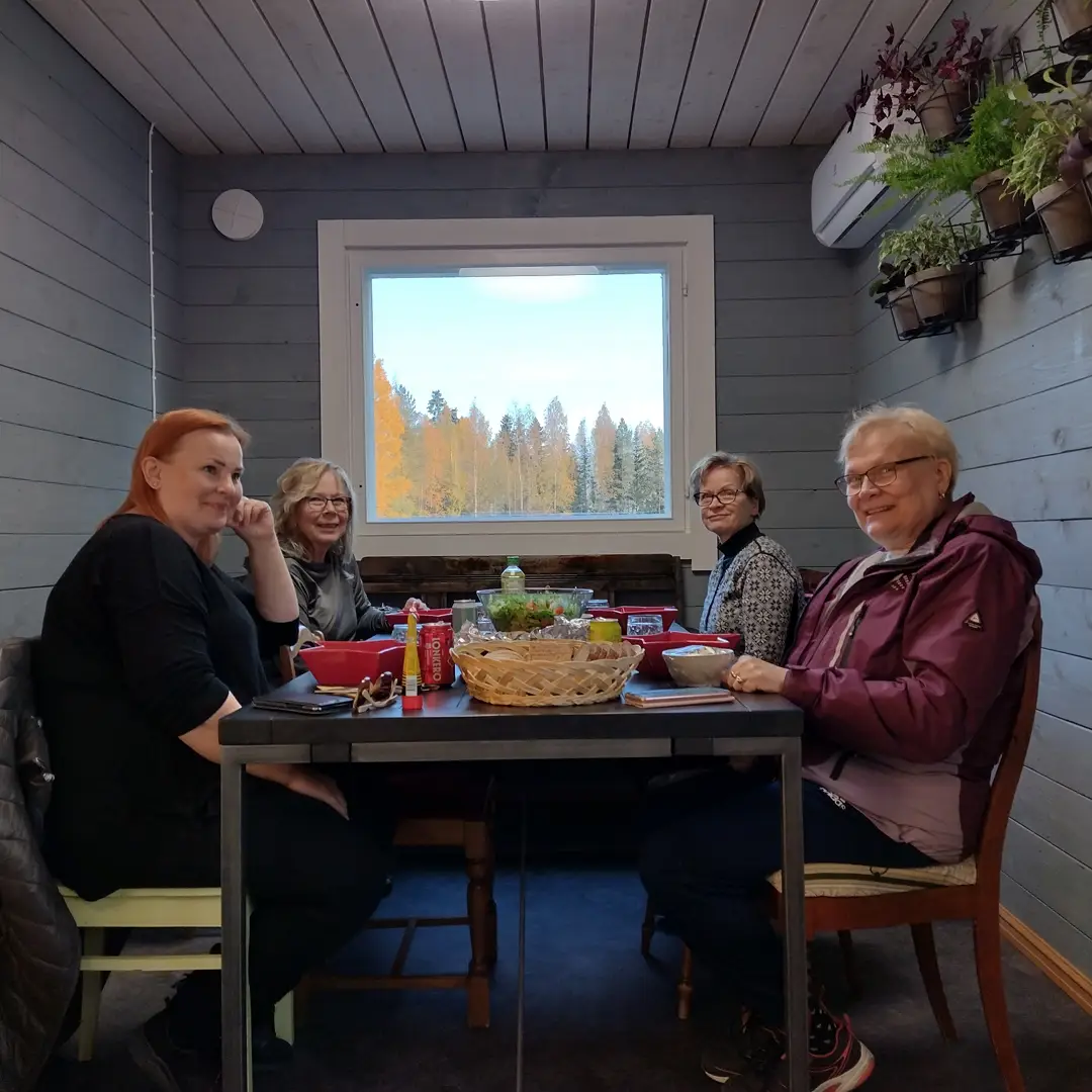 Neljä naista istuu sisällä ruokapöydän ympärillä