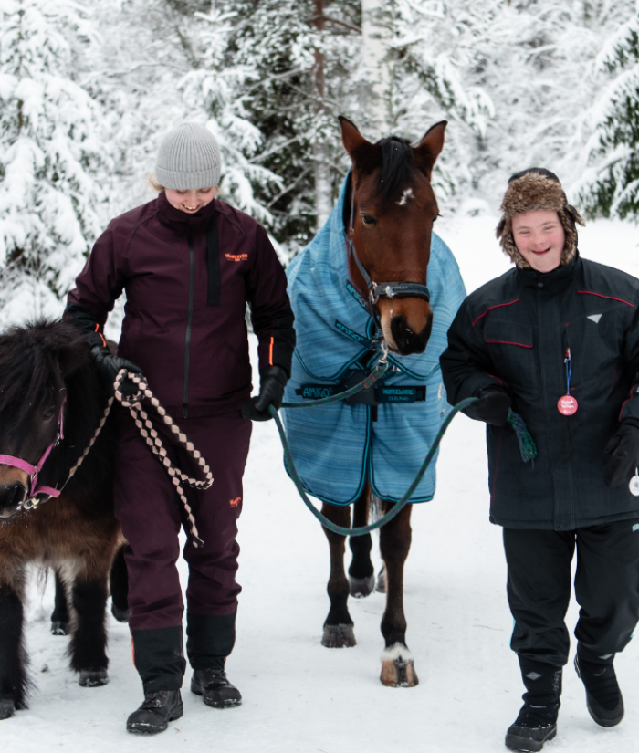 Nainen ja kehitysvammainen poika taluttavat hevosia